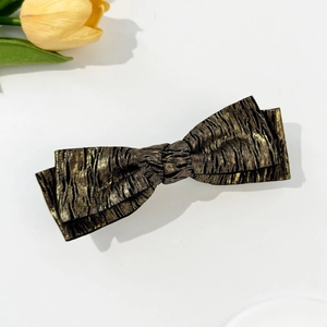 Macro shot of metallic gold and black pleated bow hair clip with textured fabric details