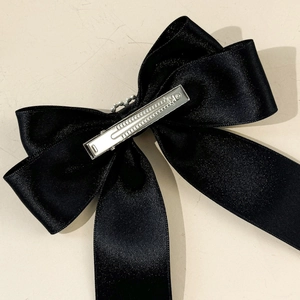 Dettaglio della clip per capelli con fiocco in raso nero e becco d'anatra in metallo