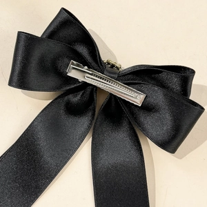 Detail view of the silver metal duckbill clip on a black satin bow hair accessory