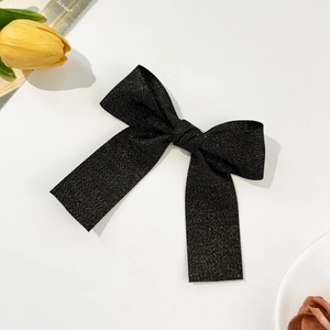 Close-up of black herringbone ribbon hair clip with gold thread and long streamers