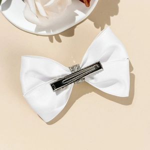 Détail d'une pince à cheveux avec nœud en satin blanc et centre en strass sur clip en métal