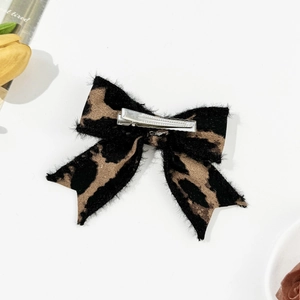 Detail of leopard print bow hair clip with silver metal alligator grip on white surface