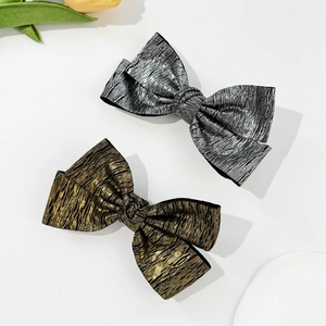 Detail of metallic textured bow hair clips in gold and silver with pleated finish