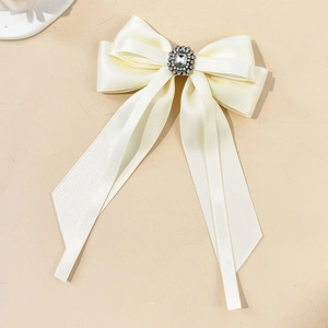 Close-up of off-white satin bow hair clip with crystal center and long flowing ribbons