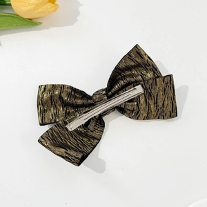Detail view of metallic gold and black wrinkled fabric bow clip with duckbill hair fastener