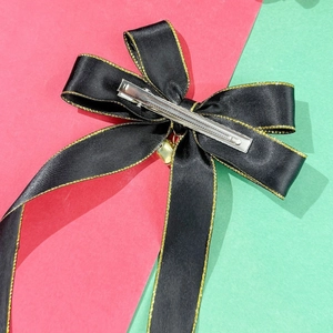 Detail view of black satin bow hair clip featuring gold trim and metal alligator clasp