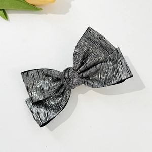 Detailed macro view of silver metallic pleated bow hair clip with textured fabric finish