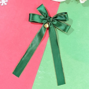 Detail of green satin bow hair clip with gold trim and a festive metal bell decoration