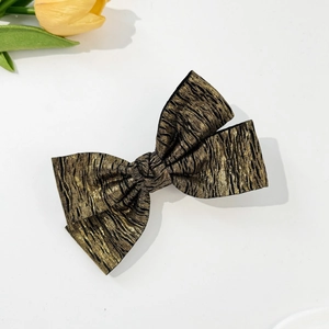 Detailed macro view of golden pleated bow hair clip with textured metallic finish