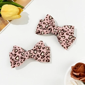Close-up of two pink leopard print bow hair clips with heart patterns on white background
