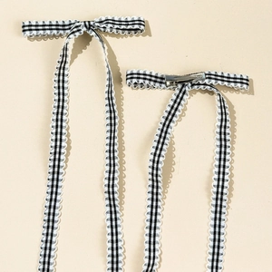 Detail view of black and white plaid bow hair clips with long ribbons and lace edges