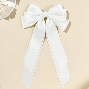 Detail of the elegant white satin bow hair clip with long ribbons on a cream background