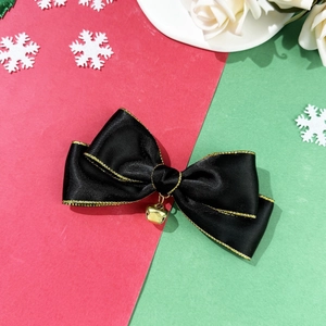 Detail of Christmas hair clip with black satin bow, golden edge, and a small metal bell