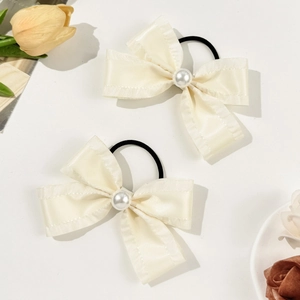 Detail view of two cream satin bow hair ties with pearl centers and elastic bands