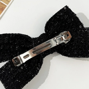 Detailed close-up of the silver metal spring clip on a black sequin bow hair clip