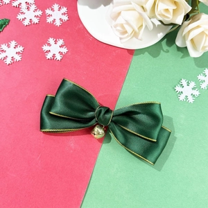 Detailed close-up of dark green satin Christmas bow hair clip with gold edges and tiny bell