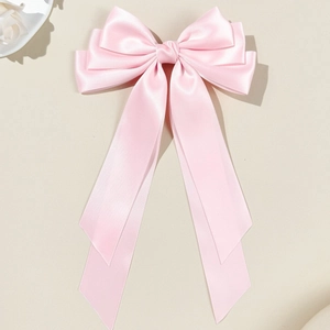 Close-up of pink satin multi-layer bow hair clip with elegant long ribbons on beige base