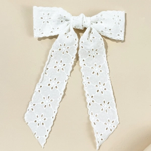 Detailed view of white lace bow hair clip with hollow floral embroidery and long ribbons