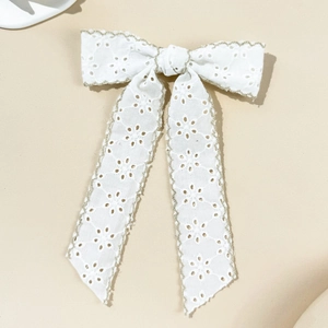 Detailed view of white lace bow hair clip with eyelet embroidery and gold stitched edges