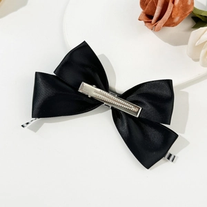 Detailed view of a black satin bow hair clip with silver metal alligator clasp