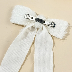 Detail of white teddy fleece bow hair clip showing the metal French barrette back