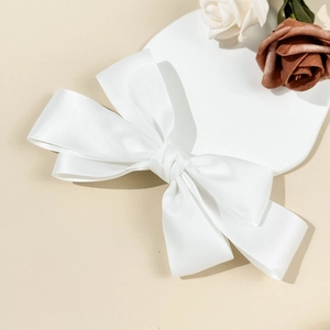 Detailed side view of a white multi-layered satin bow hair clip on a soft cream background
