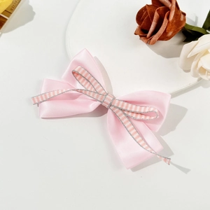Pink satin and striped ribbon bow hair clip with silver edges on a decorative tray