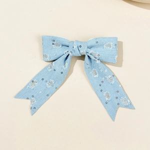 Close-up of light blue denim bow hair clip with silver sequins and frayed tassel edges