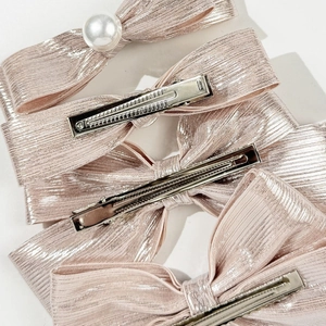 Detail view of 4-piece pink bow hair clips with glitter fabric texture and pearl accent