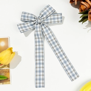 Detail of blue and white plaid bow hairclip with long ribbons on a white surface