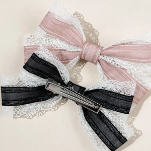 Detail of pink and black lace bow hair clips showing fabric texture and metal duckbill clips