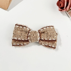Detail of tweed bow hair clip with golden sequins and brown faux fur trim accents