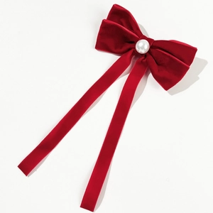 Close-up of elegant red velvet hair clip featuring a white pearl center and long streamers