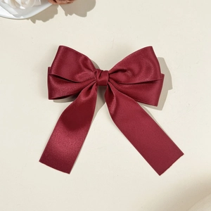 Détail du nœud de cheveux élégant en satin rouge vin avec longs rubans sur fond crème