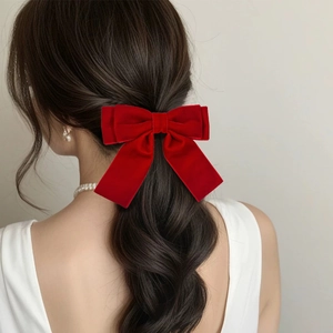 Rear view of model wearing a large red velvet bow hair clip with long flowing ribbons