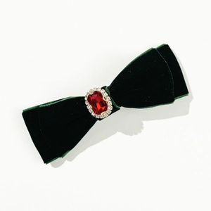 Macro shot of green velvet bow hair clip featuring a large ruby-red crystal detail