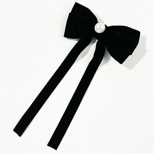Detailed macro of a black velvet bow hair clip with a large pearl center and long ribbons