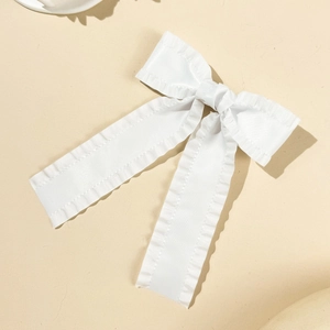 Détail d'une pince à cheveux blanche en tissu avec bords ondulés et longs rubans doux