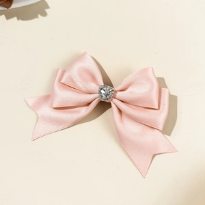 Detail einer rosa Satin-Doppelschleife-Haarklammer mit glitzerndem Strassherz in der Mitte