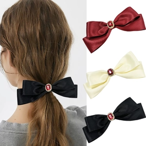 Detail view of satin bow hair clips with ruby rhinestones in black, red, and beige