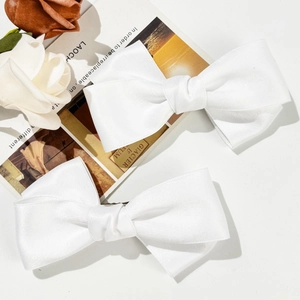 Pair of white satin bow hair clips on a minimalist background with vintage postcard