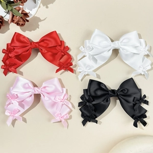 Détail de quatre barrettes à nœuds en satin rouge, blanc, rose et noir avec petits nœuds