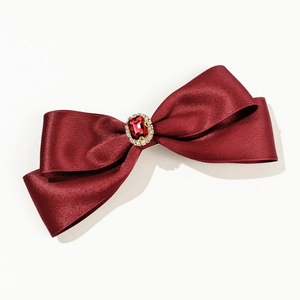 Macro detail of the red satin bow hair clip featuring a faceted ruby gemstone and rhinestones