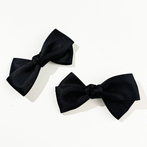 Close-up of a pair of black ribbon bow hair clips with a detailed twill fabric texture