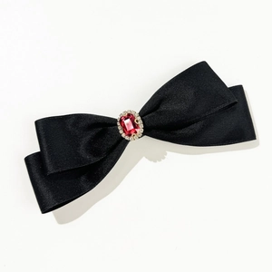 Close-up of elegant black satin bow hair clip with red ruby gemstone detail