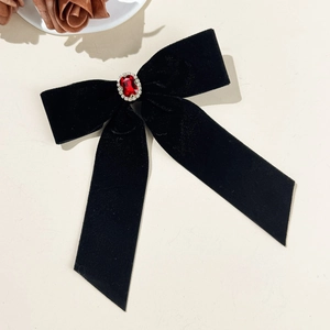 Macro detail of velvet bow hair clip featuring a ruby gemstone and rhinestone trim