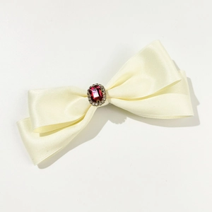 Detailed macro view of the cream satin bow hair clip with a red gemstone and crystal trim
