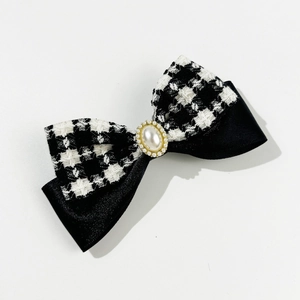 Detail view of houndstooth and black satin bow hairclip with elegant pearl center