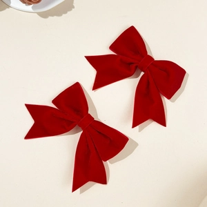 Detail of two red velvet bow hair clips with long ribbons on a cream background