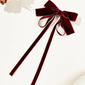 Elegant burgundy velvet bow hair clip with long ribbons on minimalist background